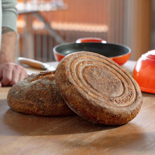 two loaves of freshly baked bread in front of a Le Creuset bread oven