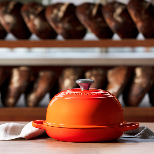 flame orange cast iron bread oven in front of loaves of fresh baked bread